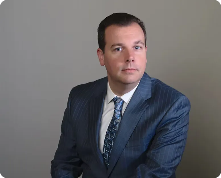 Professional portrait of a man in a blue pinstripe suit and patterned tie against a gray background.
