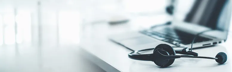 Black headset with microphone on white desk next to a partially visible laptop.