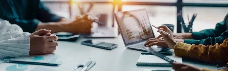 Professionals collaborating at a table with a laptop displaying colorful bar charts and documents.