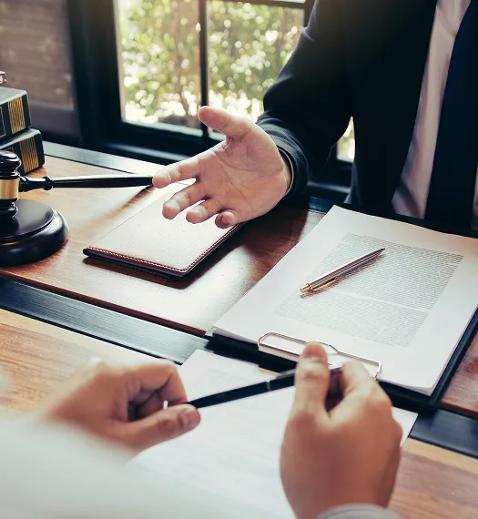 Two professionals in formal attire discussing documents at a wooden desk.