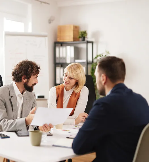 Three professionals engaged in a discussion around a table in a modern office.