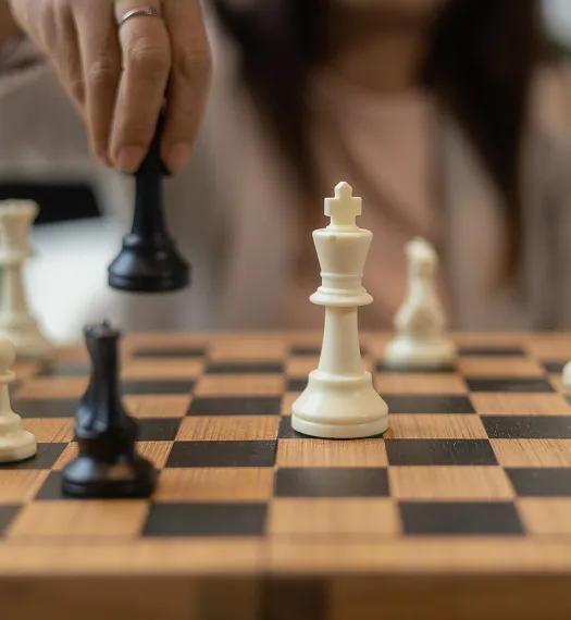Person moving a black chess piece on a wooden chessboard with white and black pieces.