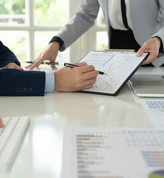 Two professionals reviewing financial charts on a clipboard in a bright office.
