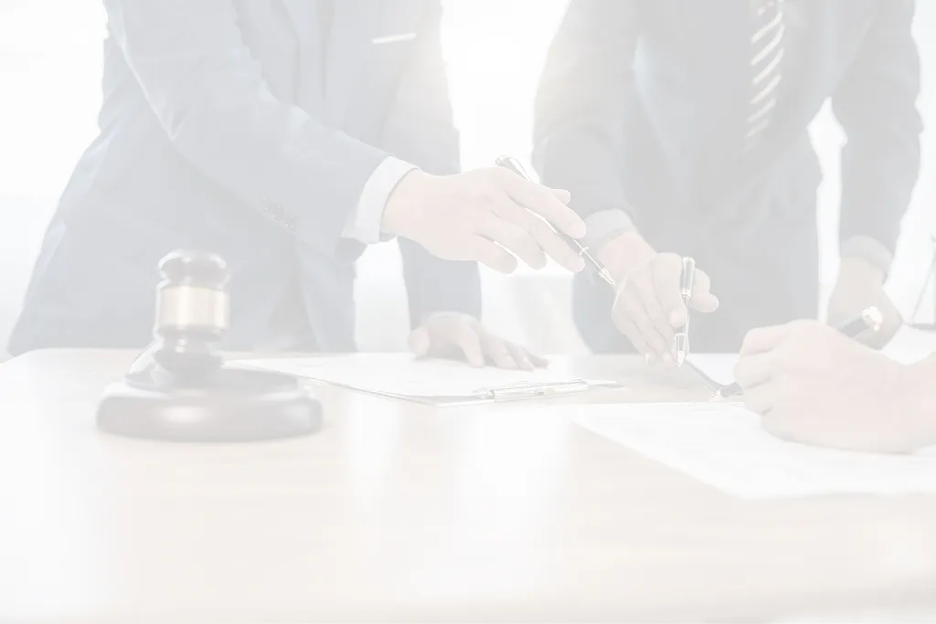 Three business professionals in suits reviewing and signing documents at a wooden table with a judge's gavel nearby.